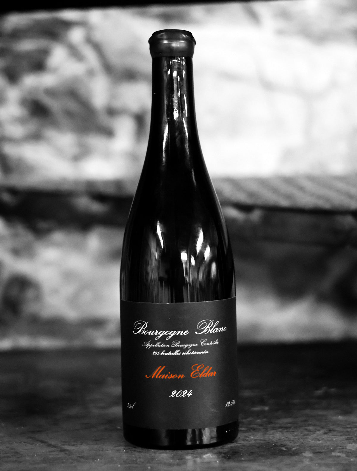 Maison Eldar Bourgogne Blanc 2024, the whole bottle on a cellar shelf, in black and white